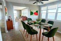 Chic dining area with green velvet chairs and glass table, showcasing modern decor and abundant natural light with stunning ocean views.