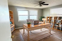 Bright and inviting home office with elegant wooden desk, chic gray chair, and ample shelving space, offering serene water views through large windows.