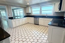Bright and spacious kitchen with stylish hexagonal tile flooring, sleek black countertops, and ample white cabinetry, complemented by large sunlit windows.
